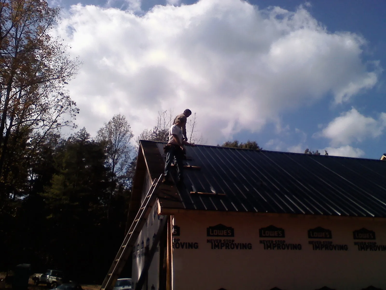 Roofer fastening dark metal panels high against a cloudy sky, from a Roof Inspection job in Ravenna